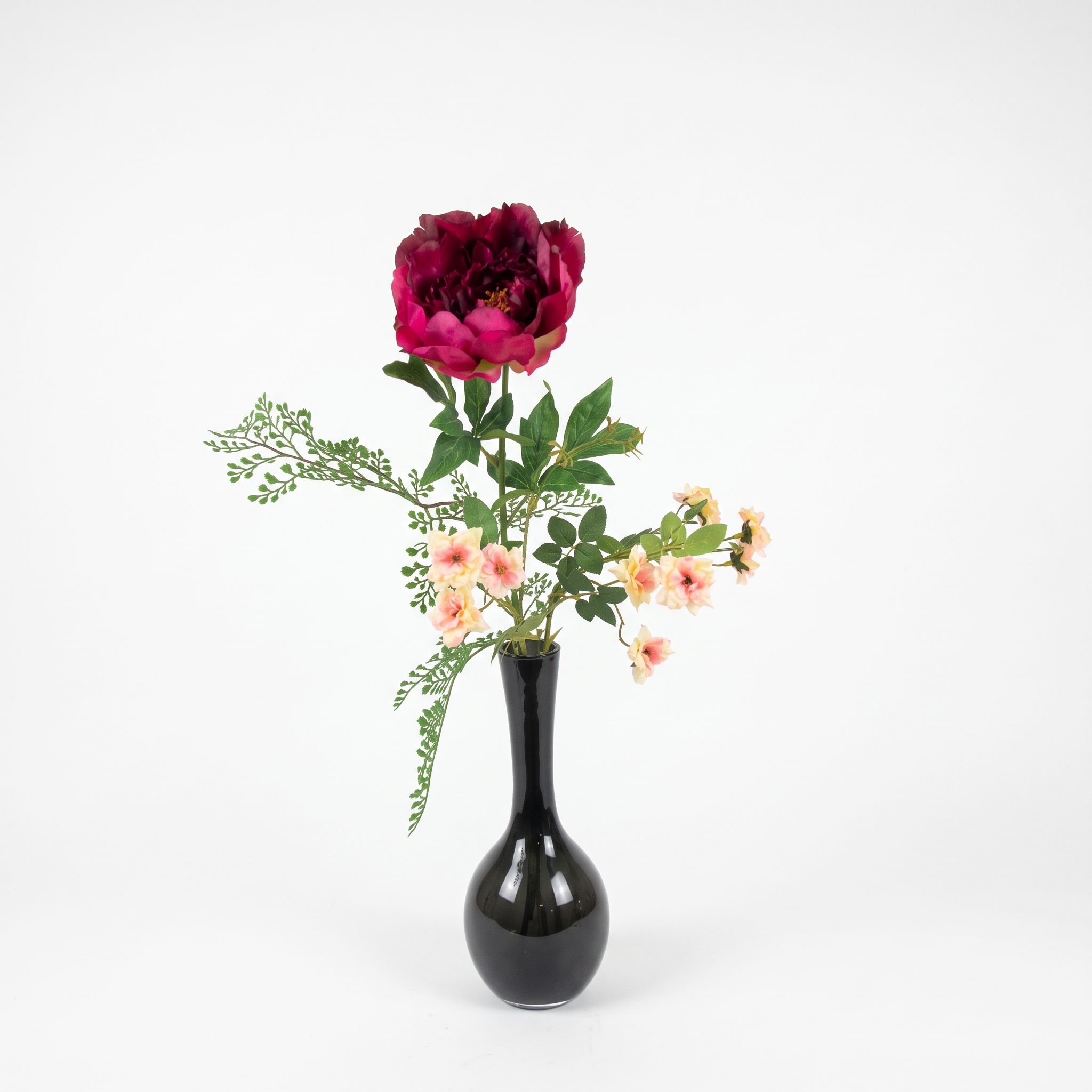 Volledig beeld van een grote donkerrode kunstmatige pioenroos en kleine roze bloemen in een zwarte vaas.