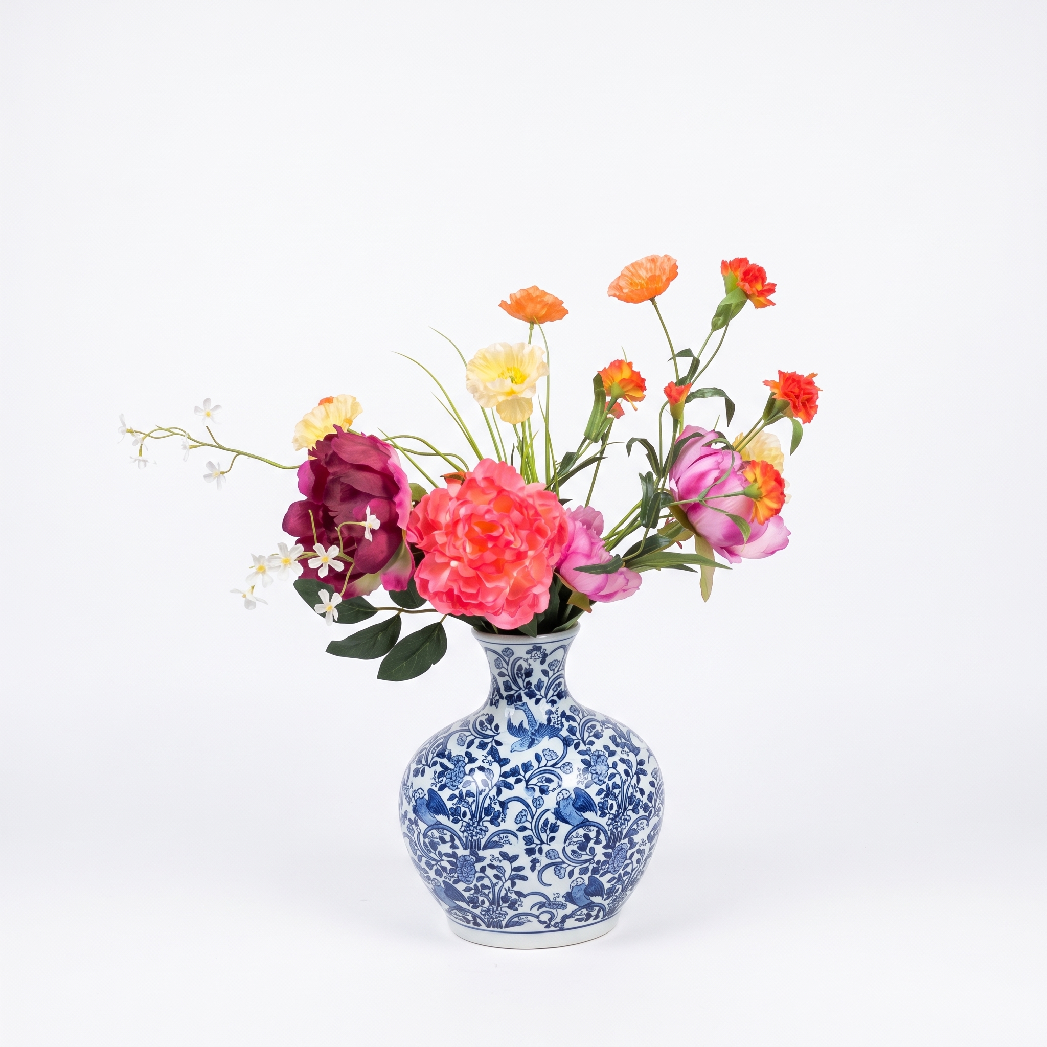 Vooraanzicht van het gemengde kunstbloemen boeket geplaatst in een gedetailleerde blauw-witte Chinoiserie vaas op een witte achtergrond.