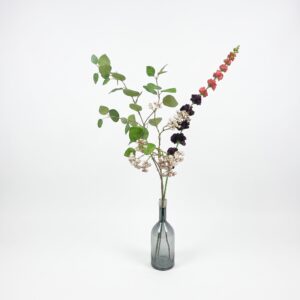 Modern zijden veldboeket met groene eucalyptus en witte duizendblad in een slanke grijze glazen vaas op witte achtergrond.